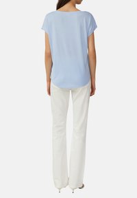 Jasnoniebieska bluzka z krótkim rękawem i okrągłym dekoltem, o miękkiej fakturze i zaokrąglonym hemie, w połączeniu z białymi spodniami w stylu dzwonów.