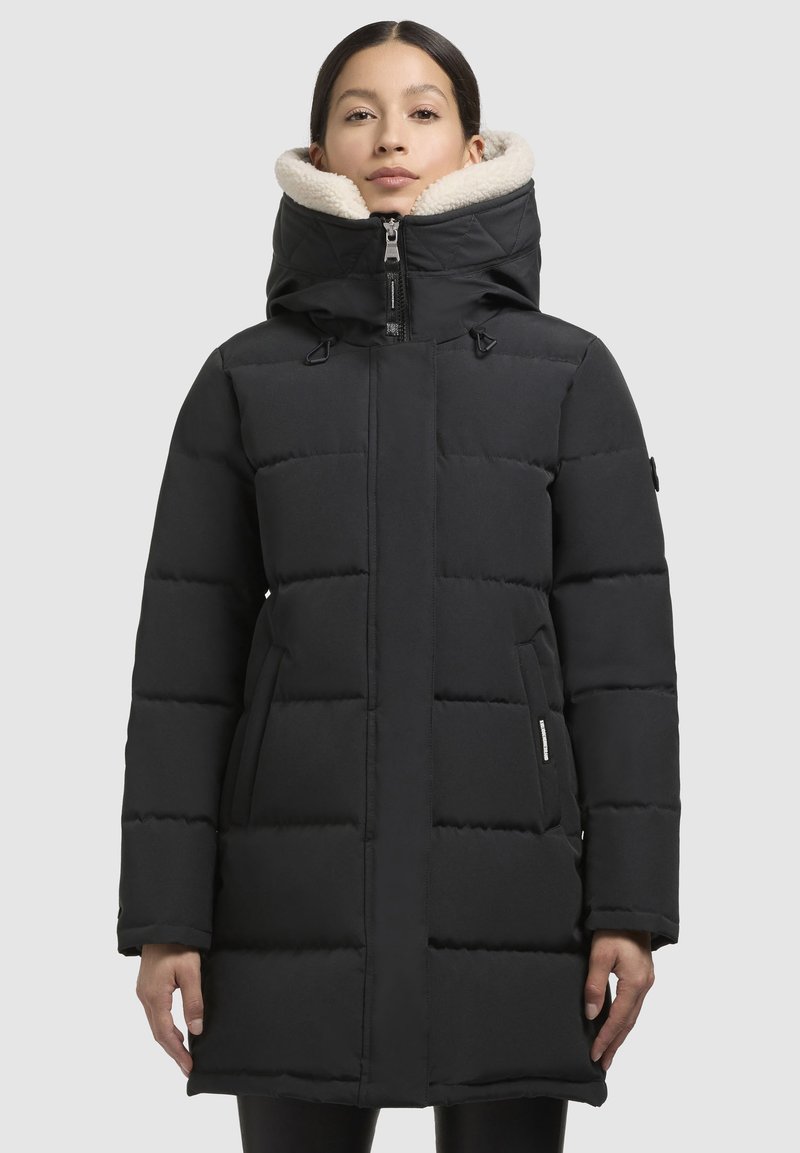 Sort pufferjakke med en fyldig hvid hætte, frontlynlås og quiltet design. Har sidelommer og justerbare snoretræk for en sikker pasform.