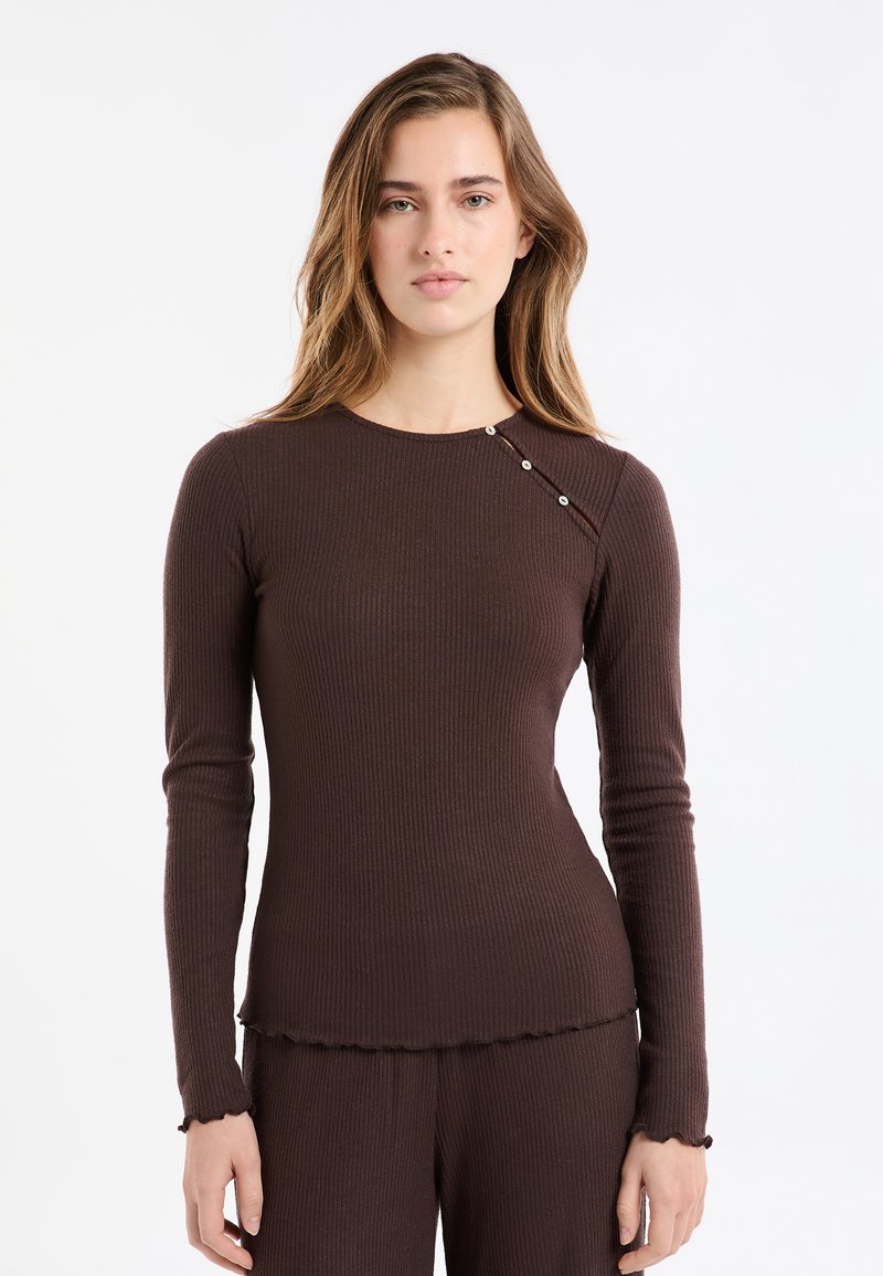 Braunes, geripptes Langarmshirt mit Rundhalsausschnitt und dekorativem Knopfdetail an der Schulter. Saum und Ärmelbündchen sind mit einem Rüschensaum versehen.