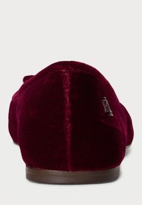 Burgundy samettimokkasiinit, joissa on sileä pinta, pyöreä muoto ja pieni metallinen logo-akseentti sivulla. Kumikäyrä tarjoaa pitoa.