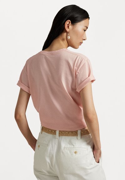 Kort rosa bomull T-skjorte med rullede ermer, rund halslinje og en avslappet passform. Båret med hvite bukser og et vevd beige belte.