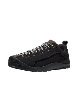 Schwarzer Sneaker in niedriger Ausführung mit weißen und schwarzen gemusterten Schnürsenkeln, Gummisohle und Stofflasche an der Ferse.