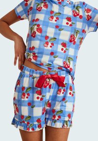 Blauw en witte geruite pyjama set met aardbeien- en kersenafdrukken. Heeft een ronde hals, korte mouwen en gerimpelde shorts met een rode strik.