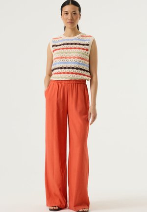 Gebreide mouwloze top met meerkleurige strepen in crème, rood, blauw en bruin, gecombineerd met wijde, elastische taillebroek in oranje.