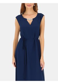 Granatowa sukienka z dekoltem w kształcie litery V i krótkimi rękawami, ozdobiona kamieniem szlachetnym przy dekolcie oraz paskiem do wiązania w talii. Gładka faktura materiału.
