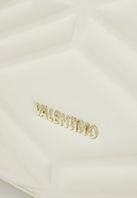 Pochette en cuir texturé blanc avec un design géométrique. Logo doré "Valentino" affiché en évidence à l'avant.