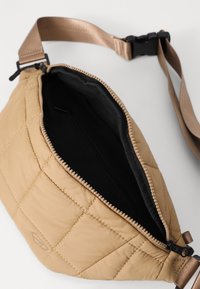 Quilted beige fanny pack with a textured surface, top zipper closure, and a black interior. Adjustable tan strap with plastic buckle.