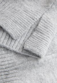 Világosszürke kötött pulóver bordázott mintával, puha anyagból készült. A szövet mintázata változó vastagságú, kellemes, otthonos megjelenésű.