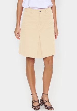 Jupe en denim beige avec une fente sur le devant, dotée de passants de ceinture et d'une fermeture à bouton unique. Assortie à des talons imprimés léopard.