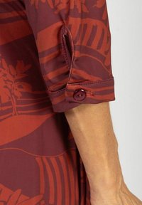 Bordo bluzka w liściasty wzór, z guzikowym mankietem i delikatnym połyskiem. Miękka, gładka tekstura i luźny krój.