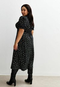 Vestido midi negro con estampado de flores, mangas abullonadas, cintura ajustada y falda fluida. Combinado con botas negras de tacón hasta la rodilla. Textura de tela suave.