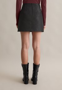 Zwarte mini-jurk met een gestructureerd bloemenpatroon, voorzien van een ritssluiting aan de achterkant. Gecombineerd met glanzende zwarte kniehoge laarzen.