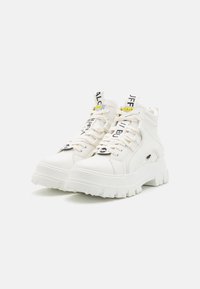Hvide høj-top sneakers med struktureret læder og en kraftig, takket sål. Har kontrasterende sort og gul branding på snørebåndene og tungen.