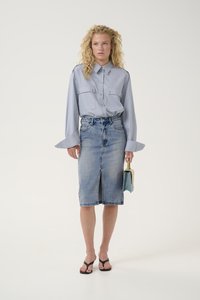 Ανοικτό μπλε πουκάμισο με δύο μπροστινές τσέπες; ψηλόμεση τζιν φούστα με μπροστινό σκίσιμο; μαύρες σαγιονάρες; κρατώντας μια μικρή μπλε τσάντα.