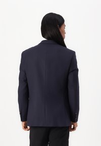 Marinblå blazer med strukturerade axlar, enkelknäppt design och knappen detaljer på ärmarna. Slät tyg med skräddarsydd passform.