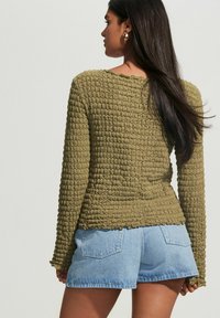 Olijfgroen gestructureerd T-shirt met lange mouwen en een golvende zoom, gecombineerd met lichtblauwe denimshorts. Eenvoudig ontwerp met minimale details.