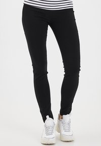 Černé elastické legíny se slim fit, doplněné o robustní bílé tenisky s šedými akcenty a tkaničkami. Textura je hladká a odolná.
