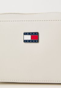 Krém színű műbőr tartó táska, kék, piros és fehér fémes Tommy Jeans logóval, finom varrási részletekkel.