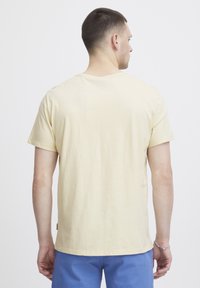 Lys gul bomulds T-shirt med korte ærmer, rund hals og lige kant. Etiketten synlig på siden. Bagfra vises.