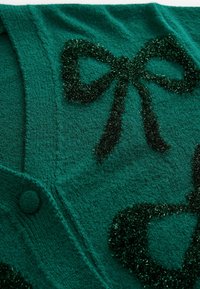 Grüner gestrickter Cardigan mit schwarzen strukturierten Schleifenmustern, weichem Stoff mit sichtbarem Stichmuster und runden Knöpfen.