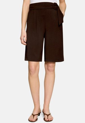 Short marron sur mesure à longueur genoux avec ceinture en tissu et boucle circulaire, porté avec des sandales marron à lanières.