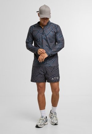 Langærmet, lynlåset top i mørkegrå med geometrisk mønster; matchende shorts med "ATW"-tryk. Båret med sneakers og en grå kasket.