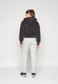 Svart cropped hettegenser med snøring, kombinert med lysegrå joggebukser. Joggebuksene har elastiske mansjetter og en avslappet passform.