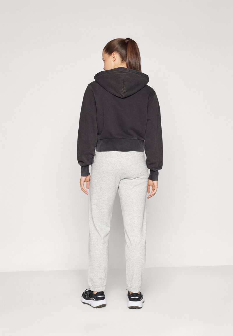 Schwarzer, verkürzter Hoodie mit Kordelzugkapuze, kombiniert mit hellgrauen Jogginghosen. Die Jogginghosen verfügen über elastische Bündchen und einen lässigen Schnitt.