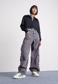 Mustat lyhyet collegepaidat, joissa on vetoketjukaulus, harmaat cargo-housut, joissa on sivutaskut, ja valkoiset lenkkarit turkooseilla yksityiskohdilla. Pehmeät ja rentouttavat tekstit.