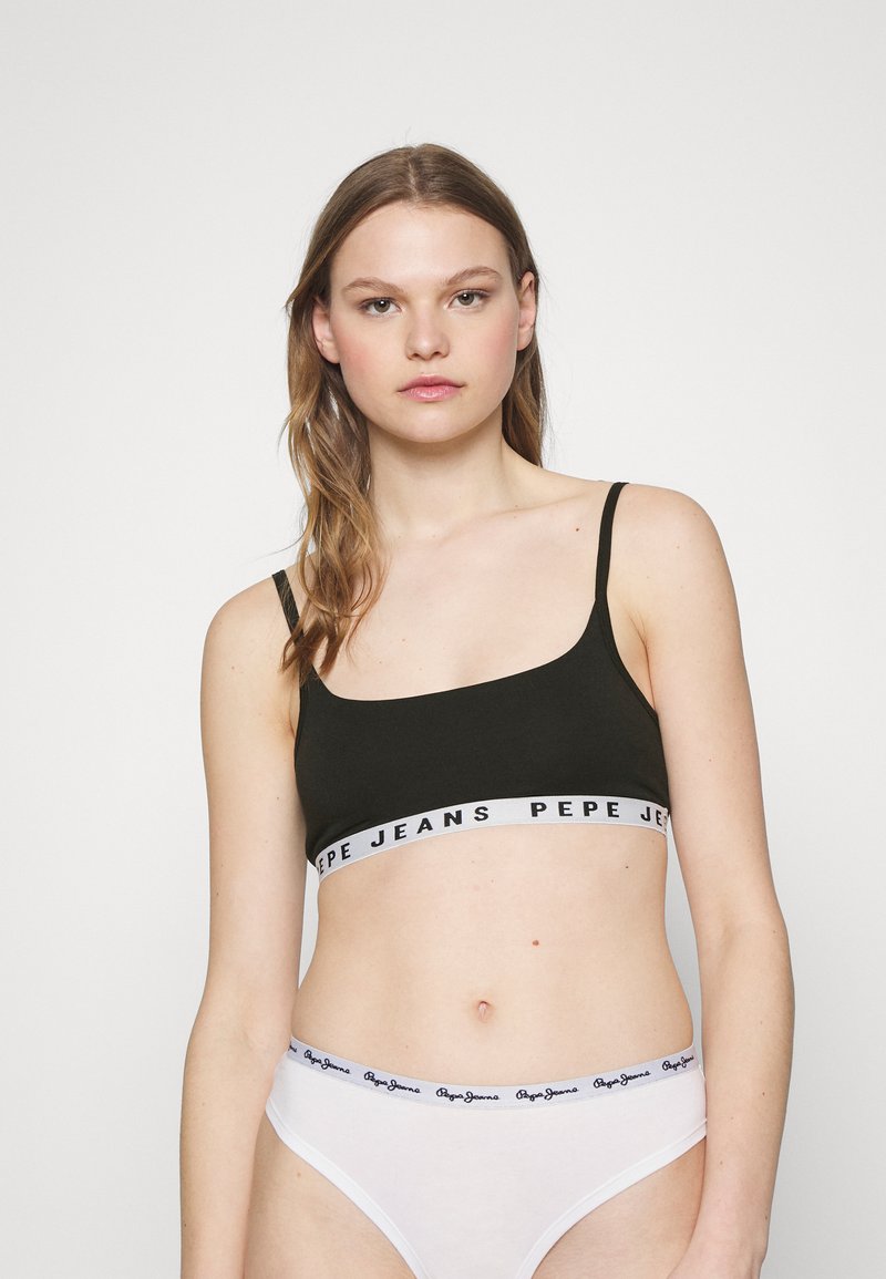 Bralette noire avec de fines bretelles, mettant en avant une bande grise contrastante avec le logo "PEPE JEANS". Associé à un bas de bikini blanc taille basse.