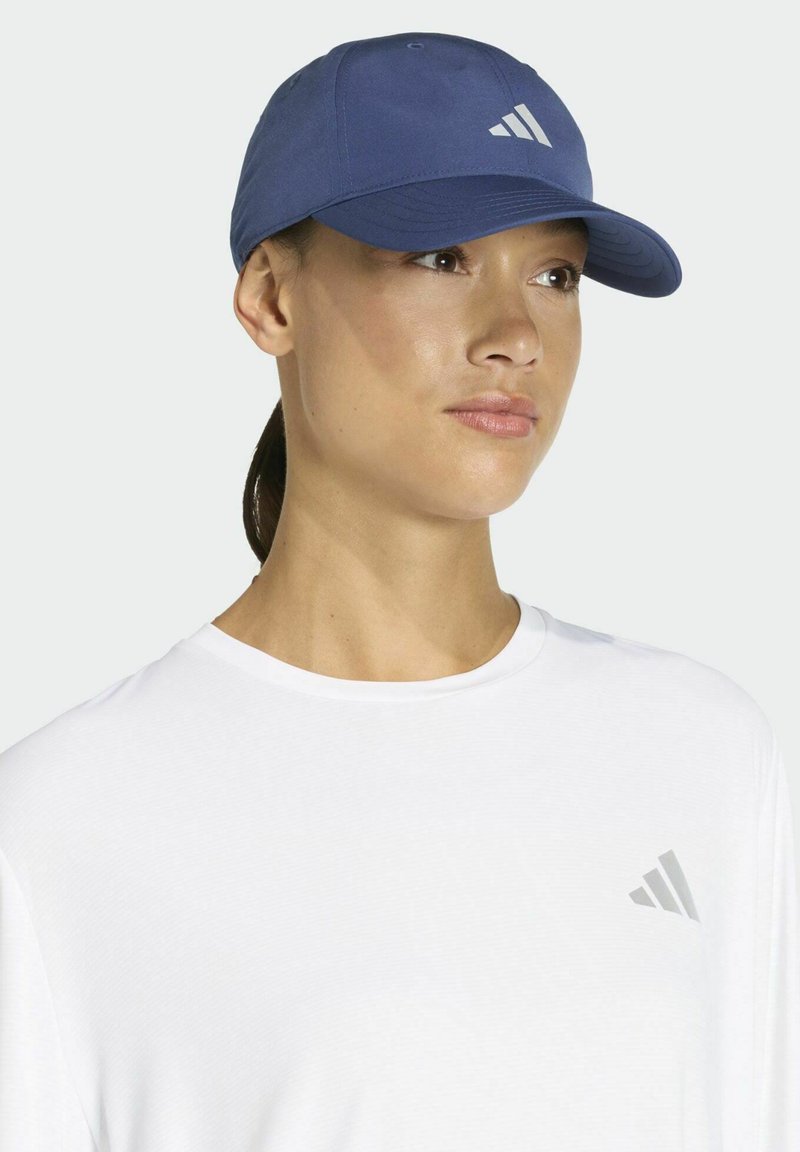 Modrá baseballová čiapka s ohnutým šiltom a bielym logom s tromi pruhmi na prednej strane, nosená s bielym tričkom so zodpovedajúcim logom.