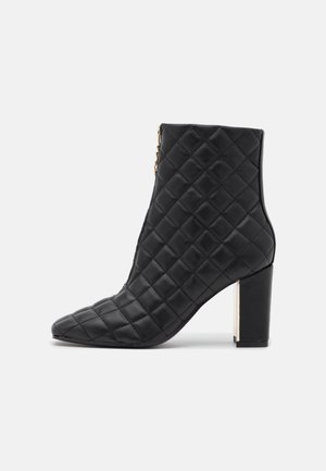 Schwarzer gesteppter Leder-Stiefelette mit Blockabsatz und Seitenreißverschluss, präsentiert vor weißem Hintergrund.