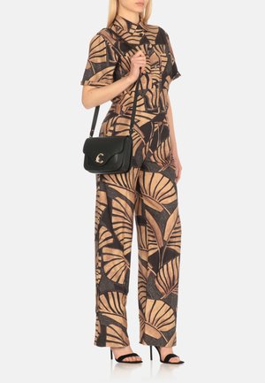 Jumpsuit con motivo a palme in beige e nero, con maniche corte e gamba larga. Abbinato a una borsa a tracolla in pelle nera.