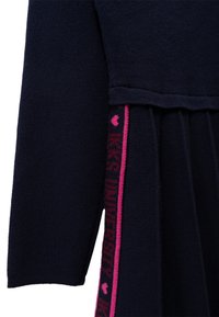 Abito lavorato a maglia blu navy con maniche lunghe, caratterizzato da una gonna plissettata e un accento a righe rosa con testo lungo il lato.