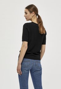 Černý pletený top s krátkým rukávem a kulatým výstřihem, ve spojení s modrými slim-fit džíny s zadními kapsami a jemnými švy.