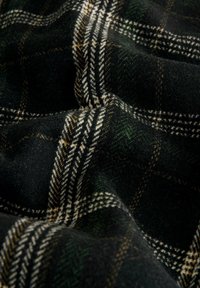 Material de lână în carouri, cu verde închis, negru și alb, accentuat cu tonuri de maro. Textură moale, cu o țesătură densă și linii de model bine definite.