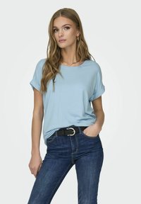 Lys blå t-skjorte med rullede ermer og rund hals, kombinert med mørkeblå jeans og et svart belte med en sølvspenne.