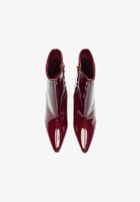 Botines de charol rojo hasta el tobillo con punta afilada y cierre de cremallera. Textura suave, diseño elegante y una silueta de tacón alto.