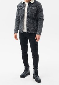 Giacca in denim nera con colletto in shearling, abbinata a pantaloni cargo neri e stivali militari neri. Le caratteristiche includono chiusure a bottone e tasche.