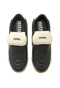 Baskets noires avec une tige synthétique texturée, une sangle blanche avec logo et une semelle en caoutchouc naturel. Comprend un rembourrage au niveau de la cheville et un renforcement à l'avant.