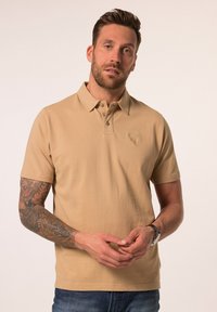 Beige polo triko s límečkem, trojím knoflíkov�ým zapínáním a decentním vyraženým logem na hrudi. Bavlněná tkanina, krátké rukávy.
