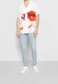 Camisa blanca de mangas cortas con un gráfico de labios rojos, combinada con jeans slim-fit de color azul claro y zapatillas blancas con suelas crema.