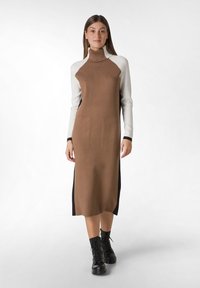 Robe en tricot avec un corps marron, des manches raglan blanches, deux poches avant et des panneaux latéraux noirs. Portée avec des bottes noires à lacets.