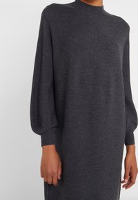 Robe grise en maille avec un col montant, des manches longues bouffantes et des poignets côtelés. Confectionnée dans un tissu doux et texturé.