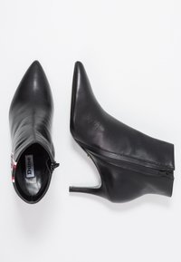 Musta nahkakengät nilkkurit, joissa on terävä kärki, stiletto-korko ja ulkopuolinen vetoketju. Sisäpuolella on merkkilogo "Dune London."