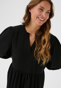 Black dress with short, puffed sleeves and a gathered waistline. Features a ruffled neckline and a V-shaped opening at the front. Textured fabric.
