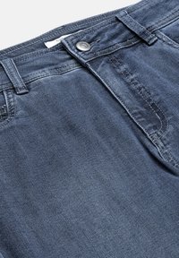 Mørkeblå denimjeans i nærbillede, der viser knap, bæltestropper og detaljer i sømmen ved forlommerne.