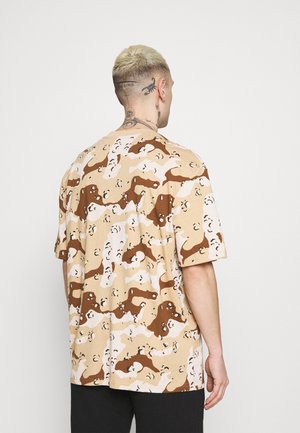Beige T-Shirt mit kurzen Ärmeln im braunen und weißen abstrakten Camouflage-Muster, mit entspannter Passform und weichem Stoff.