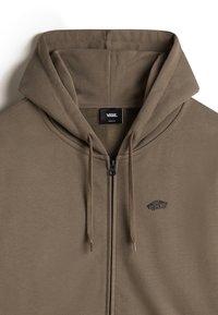 Brauner Zip-Hoodie mit einer Fronttasche und Kordeln. Zeigt ein Vans-Logo auf der Brust. Hergestellt aus weichem, strukturiertem Stoff.