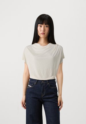 Lys beige draperet t-shirt med korte ærmer, blød tekstur, parret med mørkeblå vide jeans med standardlommer og knaplukning.